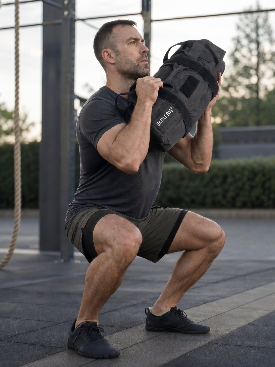 guy squating with a battle bag in a outdoor gym